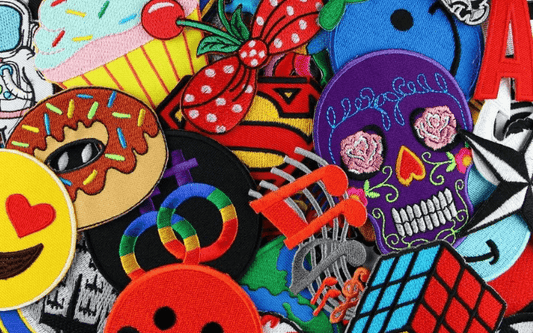 A collection of colorful embroidered patches featuring various designs including a donut, a skull, a cupcake, a Rubik's cube, and an emoji face.
