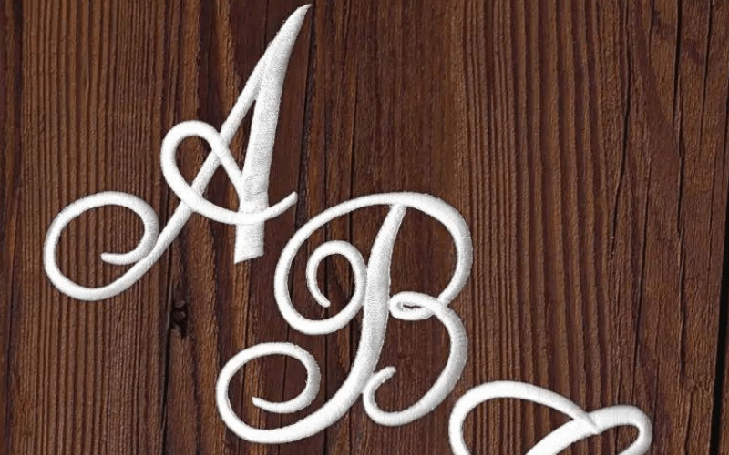 Embroidered white letters "a" and "b" in a fancy script on a dark wooden background.