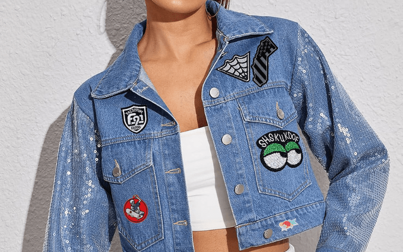 Person wearing a denim jacket with various patches and a white tube top, standing against a light gray textured wall.