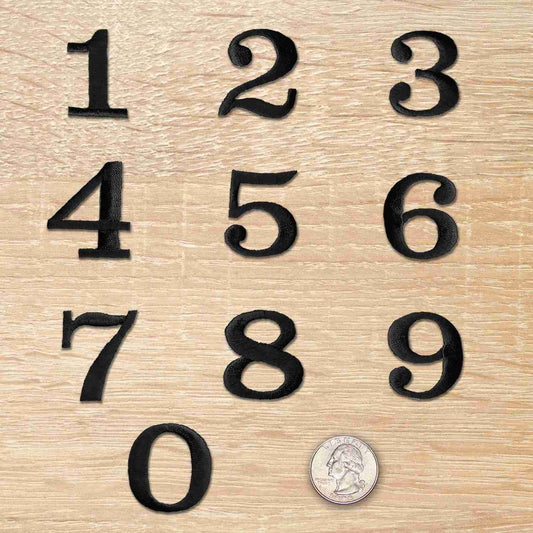 A set of Black 0-9 Numbers Iron On Patches 1-1/4"H - Sold Separately on a wooden surface.