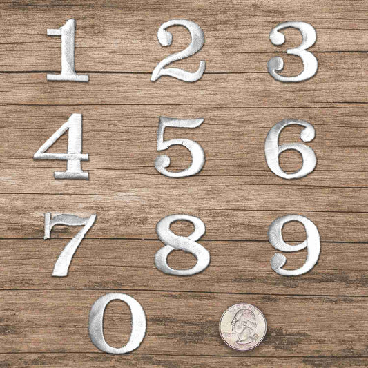 A set of White 0-9 Iron on Patch 1-1/4"H - Sold Separately on a wooden surface.