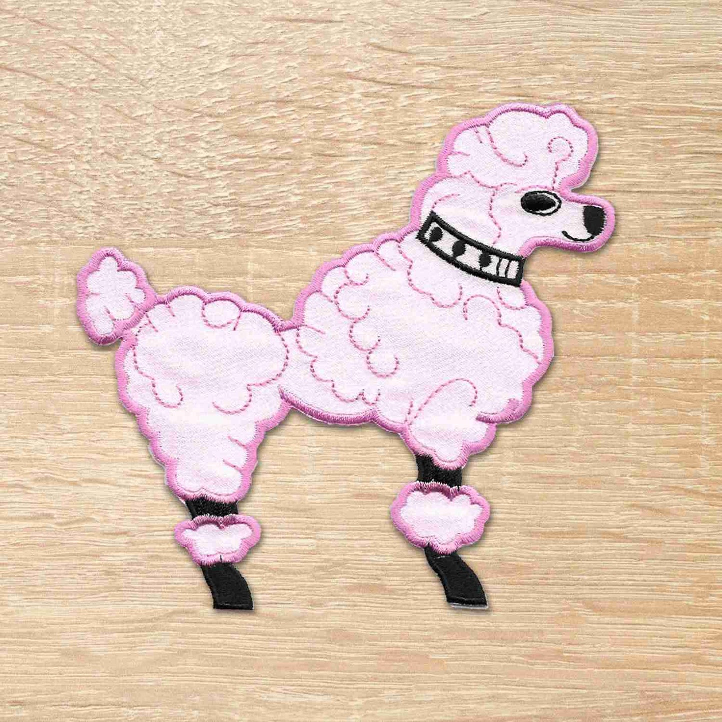 A 50's Poodle Embroidered Iron On Patch on a wooden surface.