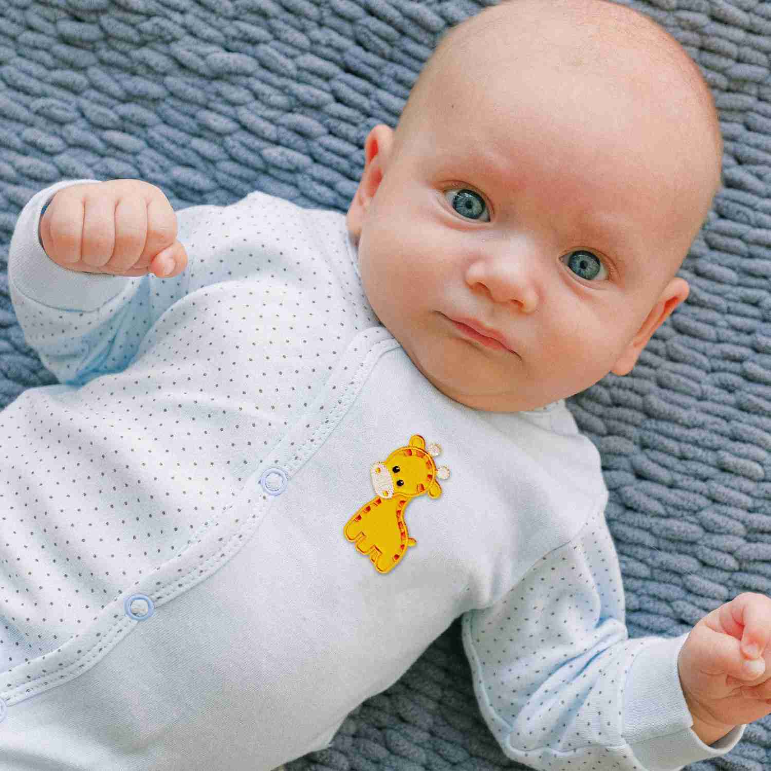 A baby laying on a blue blanket with Giraffe Patches (2 Pack) Animal Children Embroidered Iron On Patch Appliques on it.