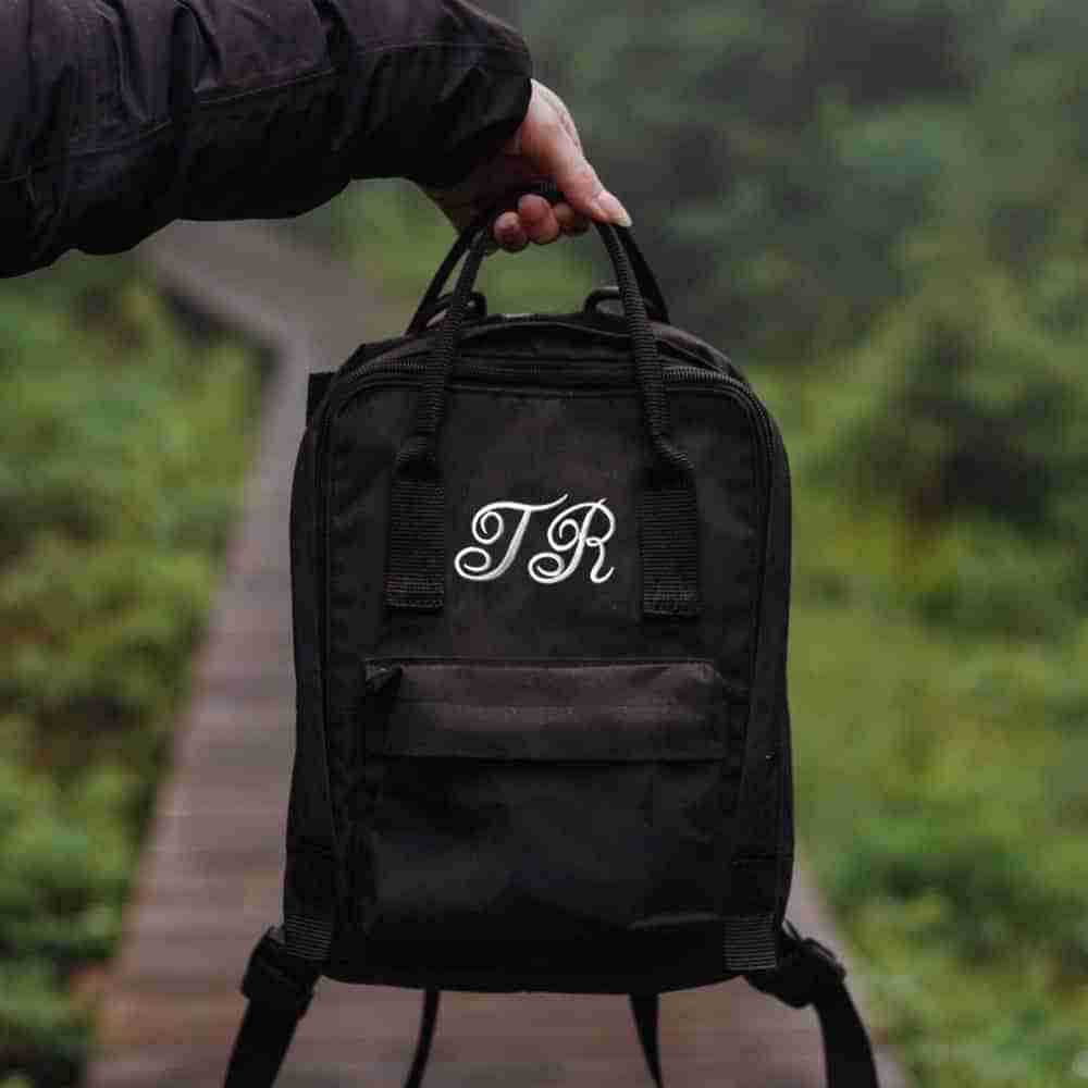 A person holding a black backpack with Iron On Script Letter Patches, Monogram Appliques on it.