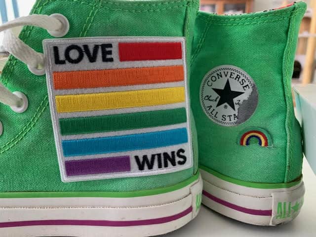 A pair of green shoes featuring Laughing Lizards’ Love Wins Equality (2-Pack) iron-on patch and a small embroidered rainbow on the heel.