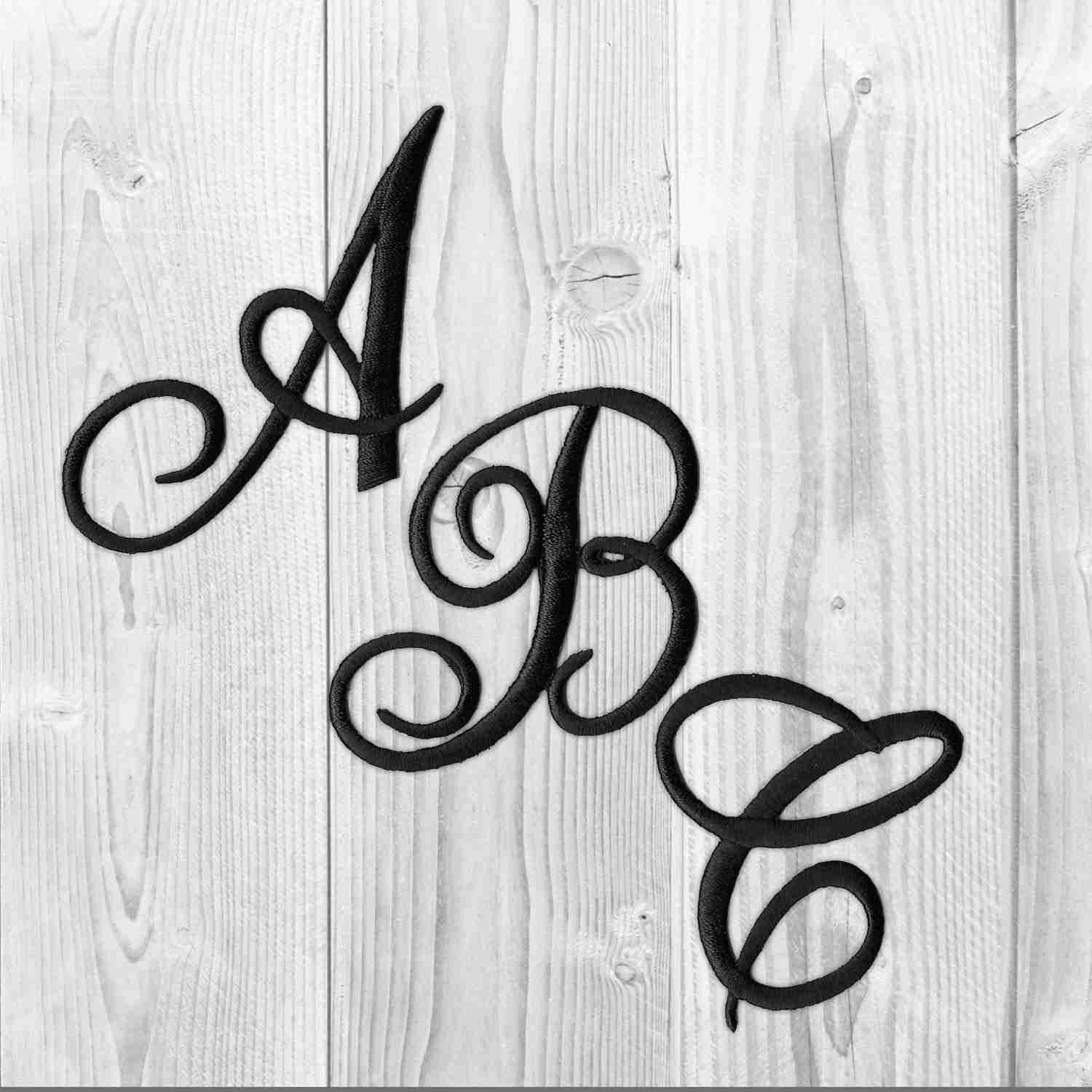 A black Iron On Script Letter Patches, Monogram Appliques on a wooden background.