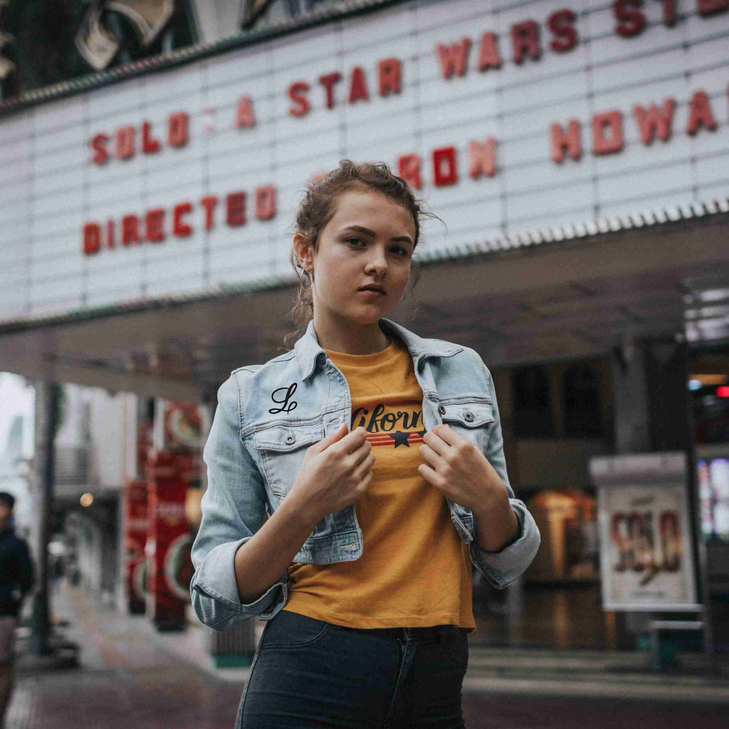 A girl wearing Iron On Script Letter Patches, Monogram Appliques t -shirt in front of a movie theater.