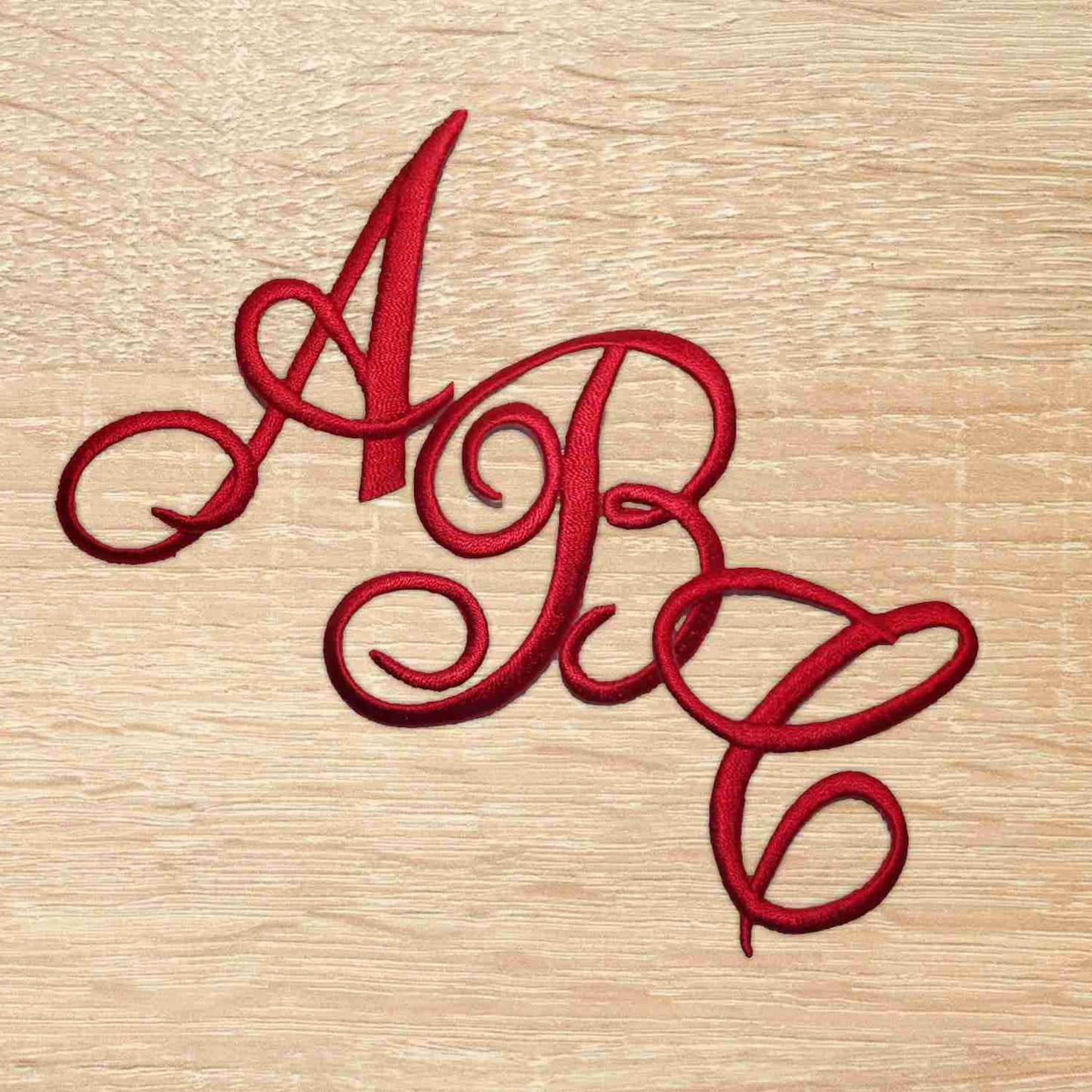 A red Iron On Script Letter Patches, Monogram Appliques on a wooden surface.