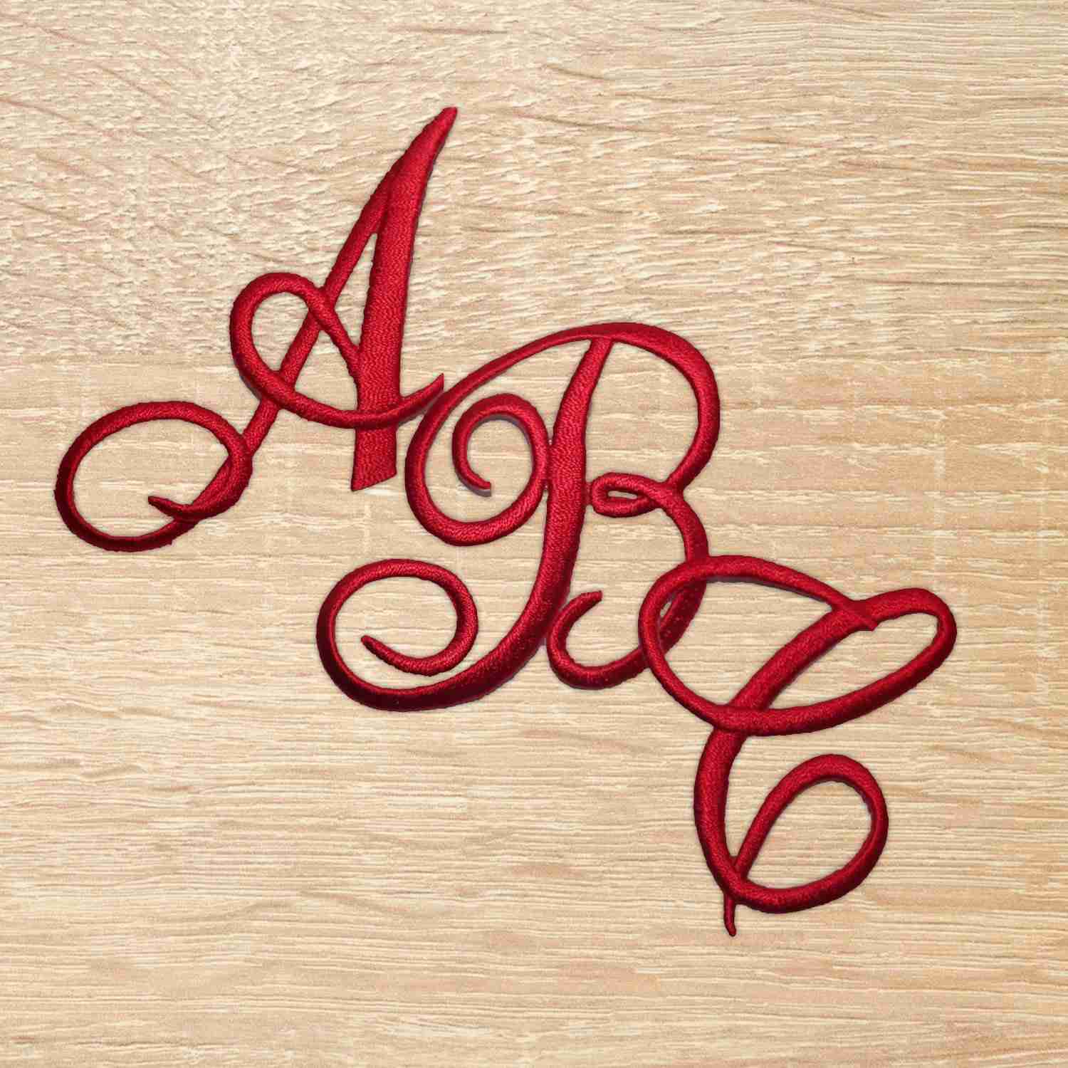 A red Iron On Script Letter Patches, Monogram Appliques on a wooden surface.