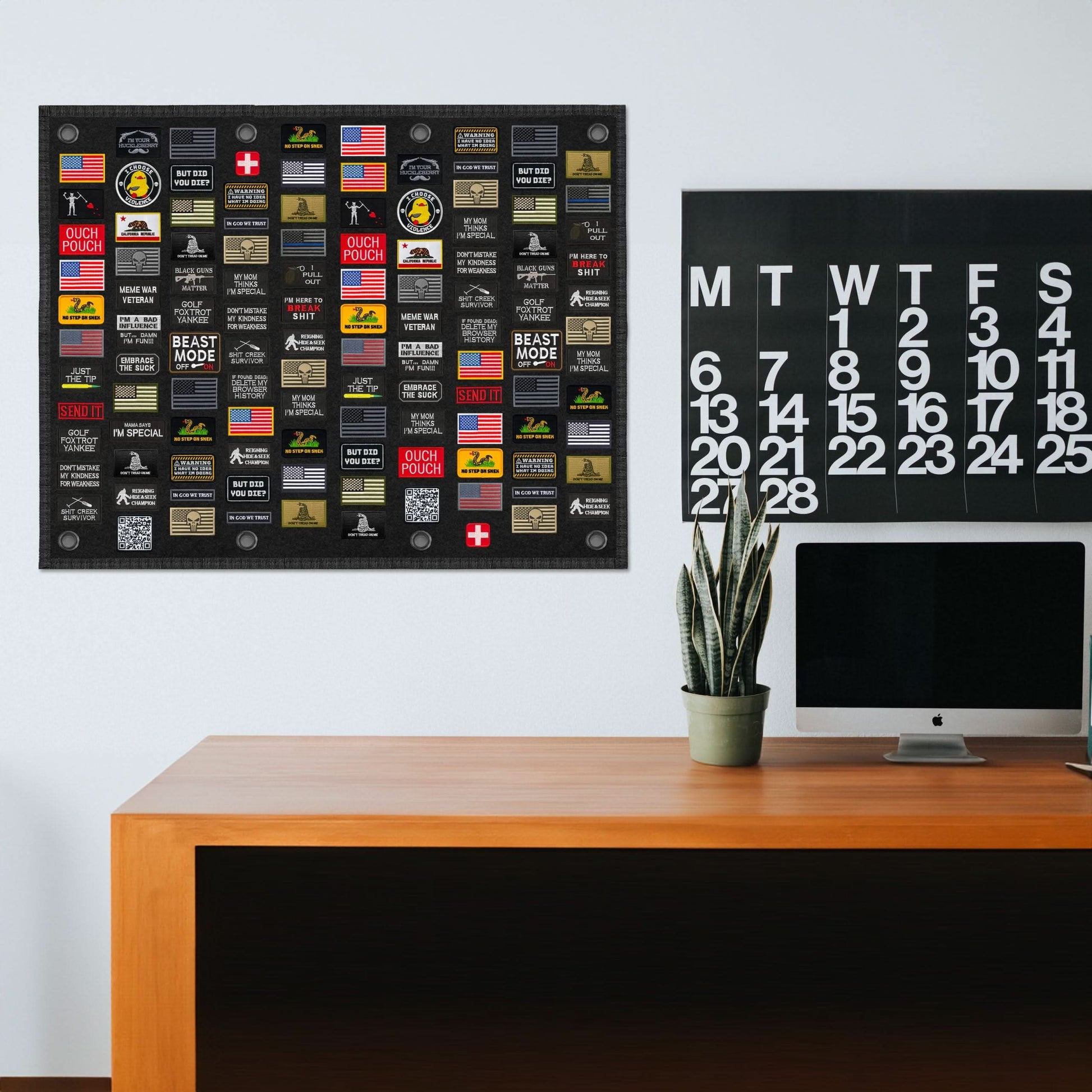 A minimalist home office with a desk, an iMac, a calendar, and a Tactical Patch Display Board Holder featuring various patches.