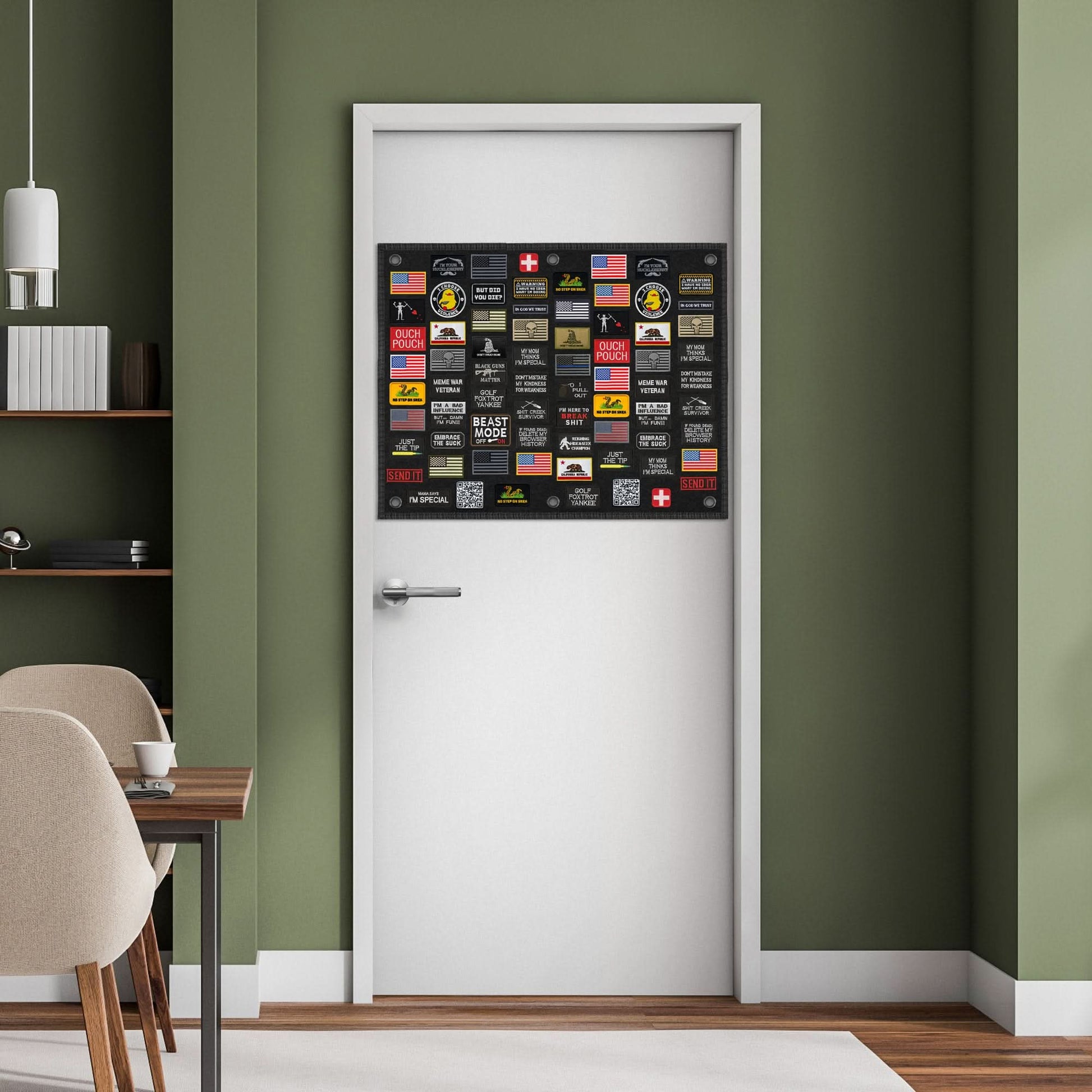 A Tactical Patch Display Board Holder for Military Army Combat Uniform Morale Emblems, Hook and Loop, adorned with an array of colorful patches and emblems, is mounted on a white door. This setup is positioned against a green wall with a bookshelf to the left and partially visible light-colored dining table and chairs in the background.