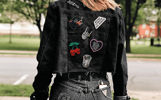 A woman wearing a black denim jacket with patches on it.