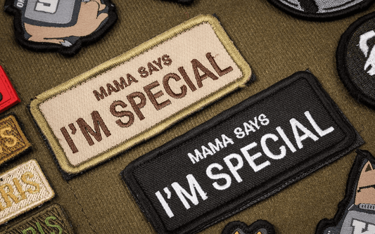 Image of two embroidered patches on fabric. The patches read "MAMA SAYS I'M SPECIAL." One patch is in tan and the other in black. Additional patches are partly visible around them.