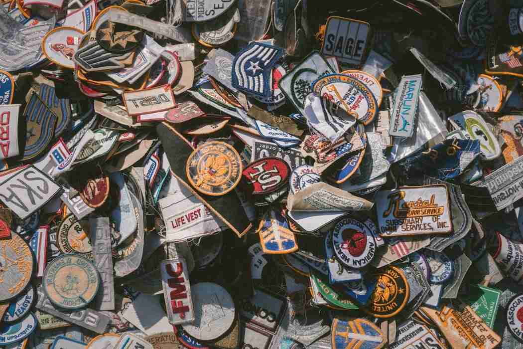 A large pile of assorted embroidered patches with various designs, logos, and text, stacked closely together.