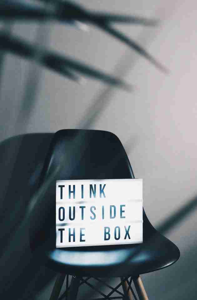A black chair with a lightbox sign placed on it displaying the words "Think outside the box" in bold letters.
