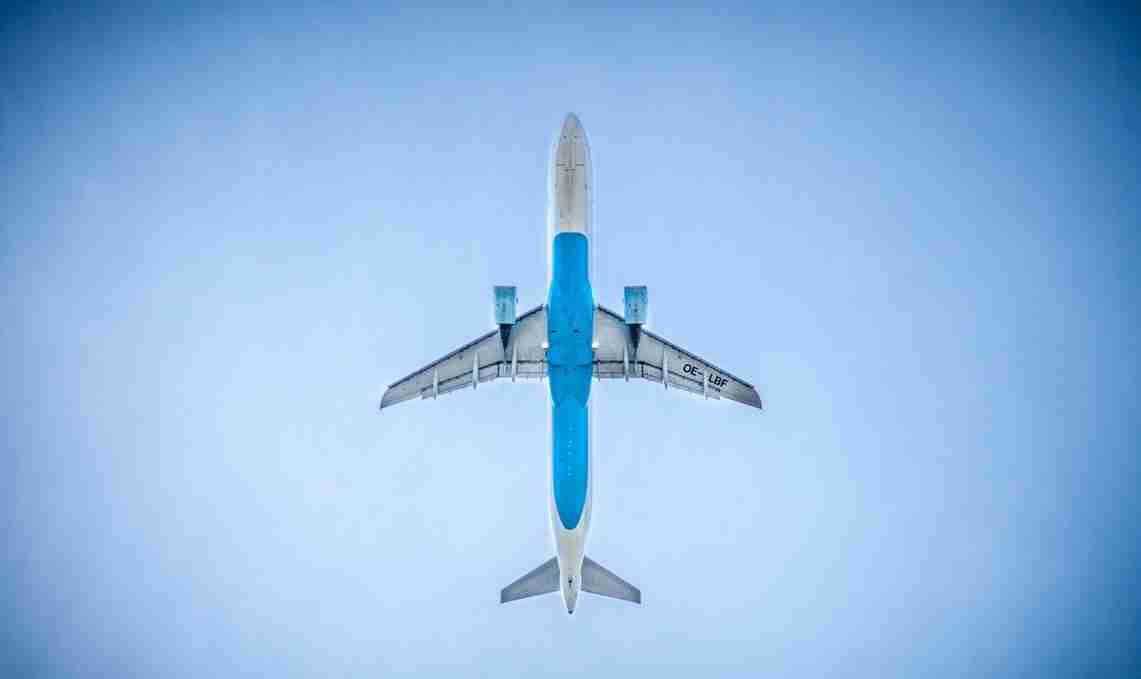An airplane with a blue and white color scheme is seen flying overhead against a clear blue sky, captured from directly below.