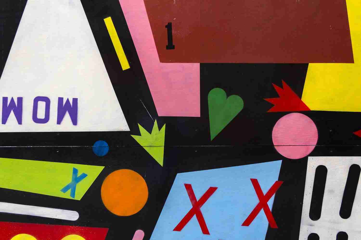 Abstract mural with geometric shapes, letters, numbers, and symbols in bold colors including red, green, blue, pink, orange, yellow, and white on a black background.