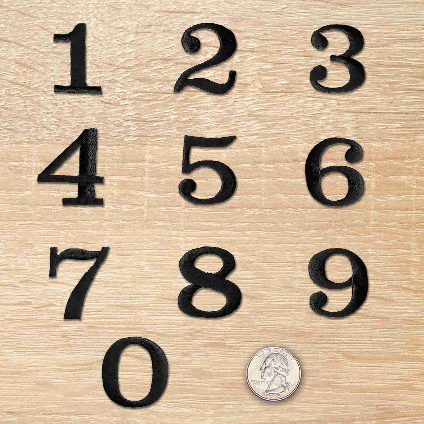 A set of Black 0-9 Numbers Iron On Patches 1-1/4"H - Sold Separately on a wooden surface.
