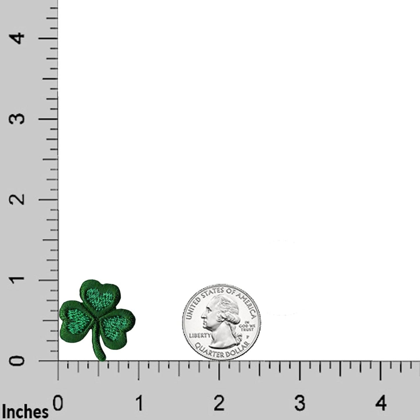 A Laughing Lizards Shamrock Patch from the 10-Pack St. Patrick’s Day Embroidered Iron On Applique is shown next to a U.S. quarter on an inch-marked grid for size comparison—great for Saint Patrick's Day crafts.