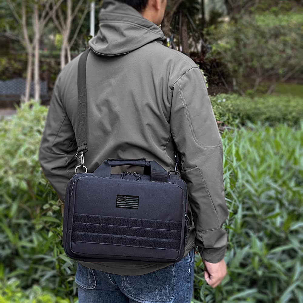 A person with a gray jacket and blue jeans carries a black shoulder bag featuring a Laughing Lizards Black & Gray USA Flag Embroidered Patch, standing outdoors near greenery.