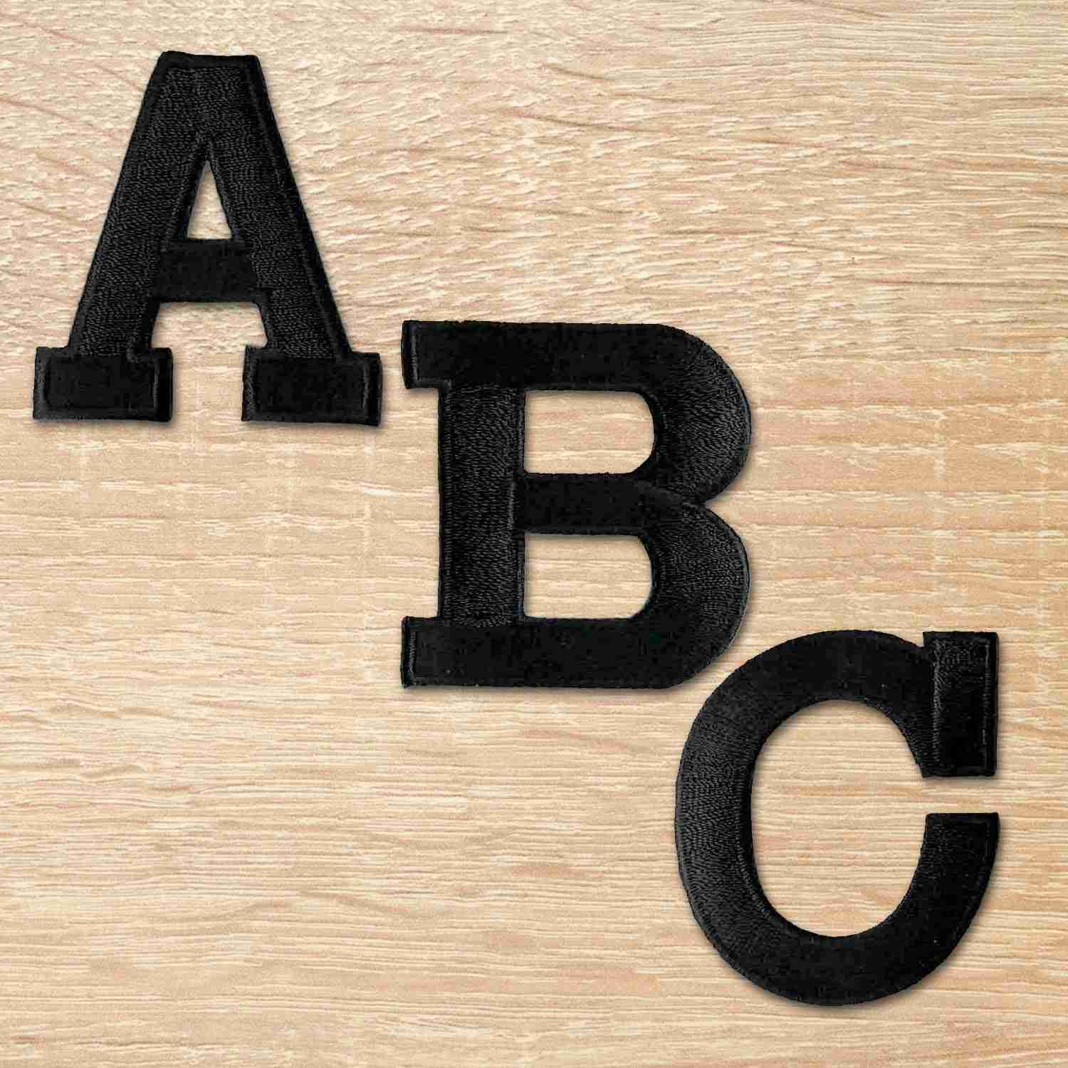 A set of Iron On Letter Patches, 2" Block Letters & Numbers on a wooden surface.