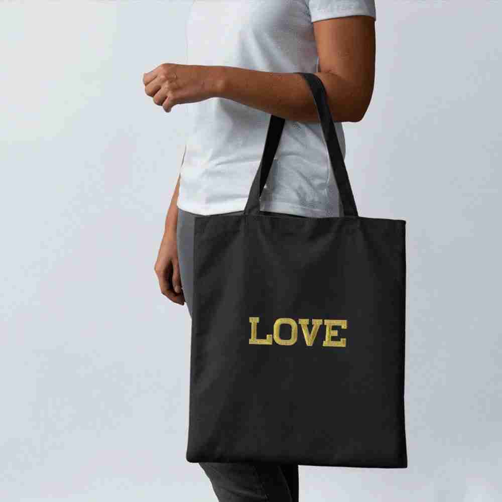 A woman holding a black tote bag with Iron On Letter Patches, 2" Block Letters & Numbers on it.