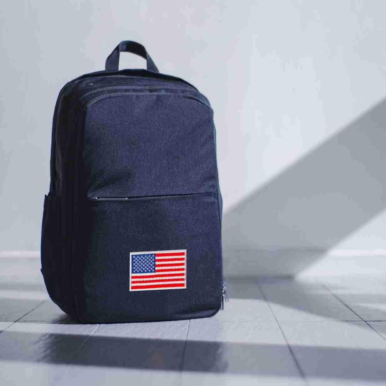 A black backpack with USA Flag Patches (2-Pack) American Flag Embroidered Iron On Patch Appliques on it.