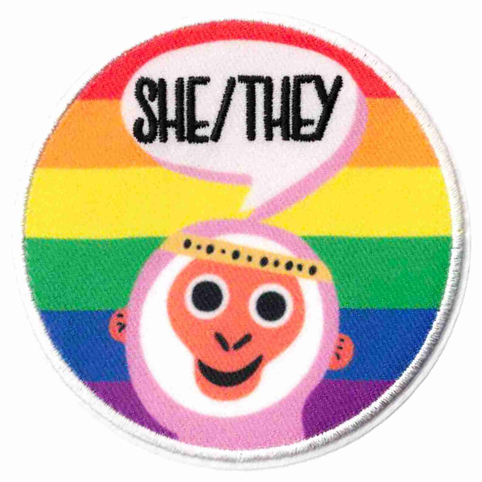 A round patch with the words She/They on it.