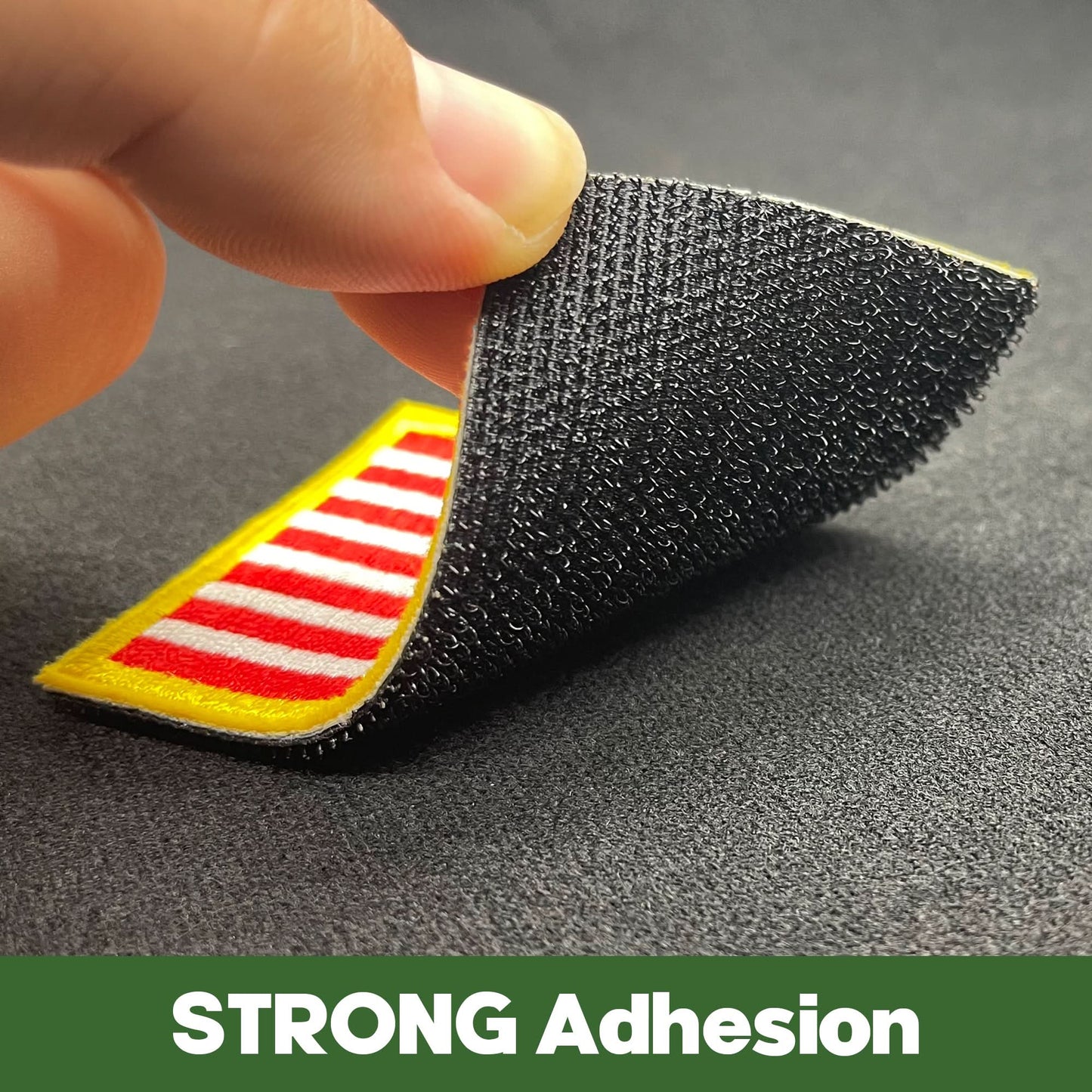 A hand peeling back a corner of a Tactical Patch Display Board Holder with hooks, revealing its yellow and red striped underside. The text "STRONG Adhesion" is displayed at the bottom.